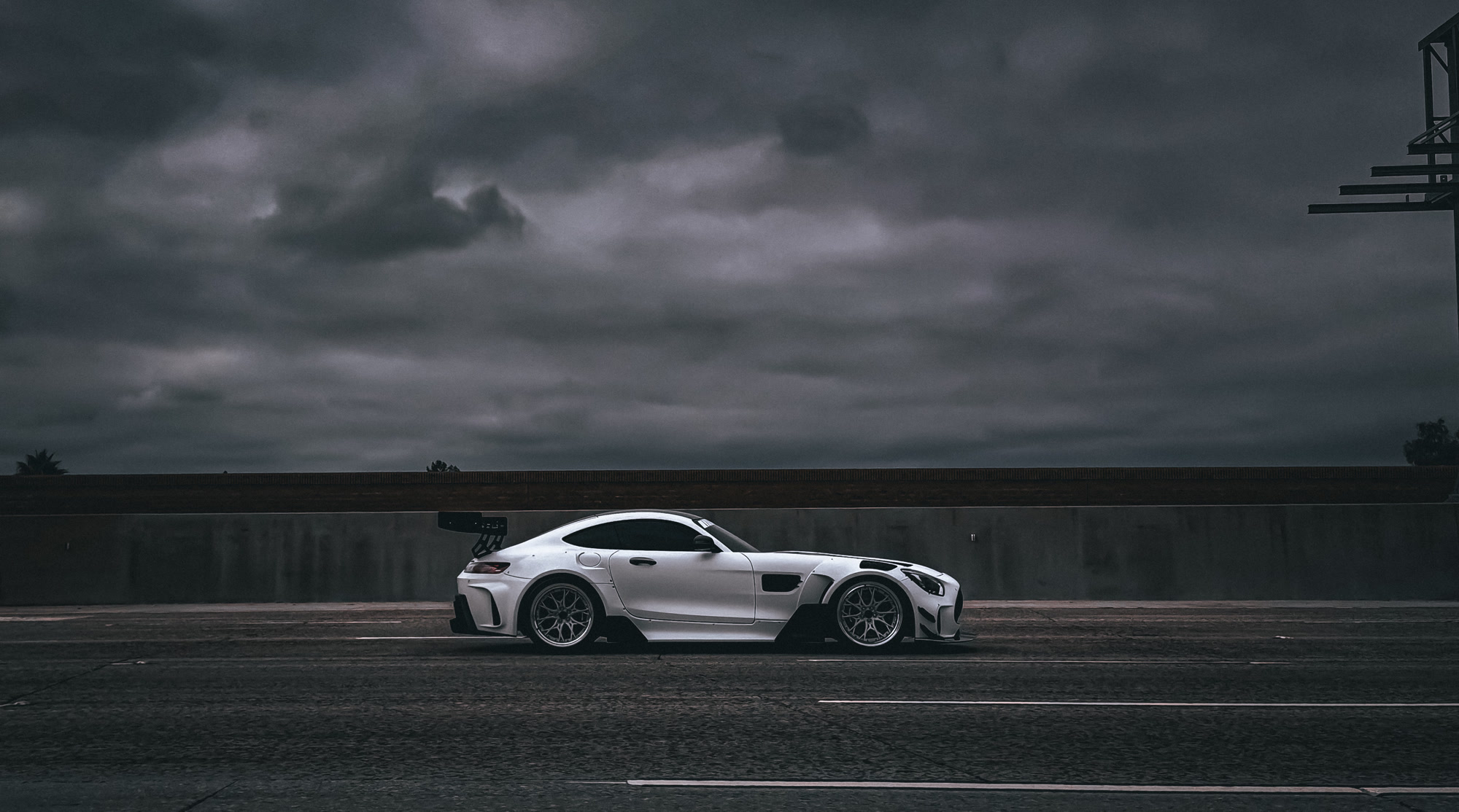 White widebody Mercedes coupe beneath a dramatic cloudy sky