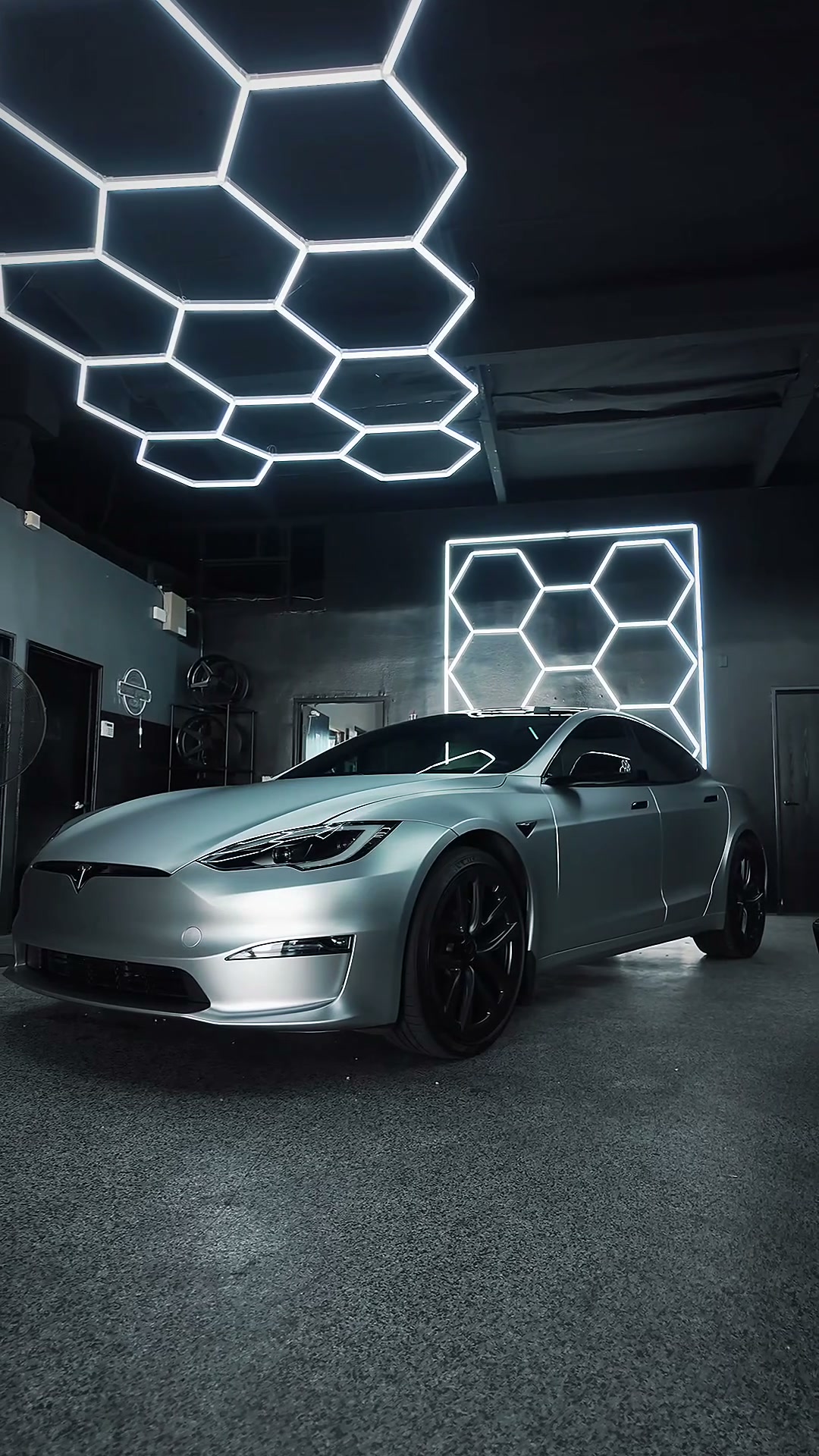 Satin silver Tesla sedan beneath the shop’s hexagonal lights
